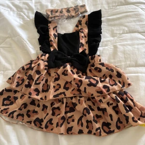 Leopardmönstrad klänning med volanger och ett hårband 3-6 månaders bebis - Söt leopardmönstrad klänning med volanger och matchande hårband. Klänningen har svarta axelband med volangdetaljer och en rosett framtill. 3-6 månaders bebis. Helt oanvänd 