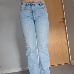 Ljusblå jeansbyxor - Säljer ett par klassiska ljusblå jeansbyxor med hög midja och rak passform. Perfekta för en avslappnad stil. De har en knapp och dragkedja framtill.