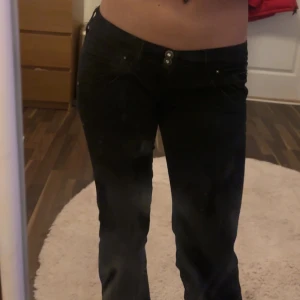 Svarta bootcut jeans från Guess - Snygga svarta jeans från Guess med låg midja och tight passform. Byxorna har klassiska femficksdetaljer och knappar framtill. Perfekta för en stilren look. höftmått: 85 midja: 70 mått tvärs över: 41 innerben: 80