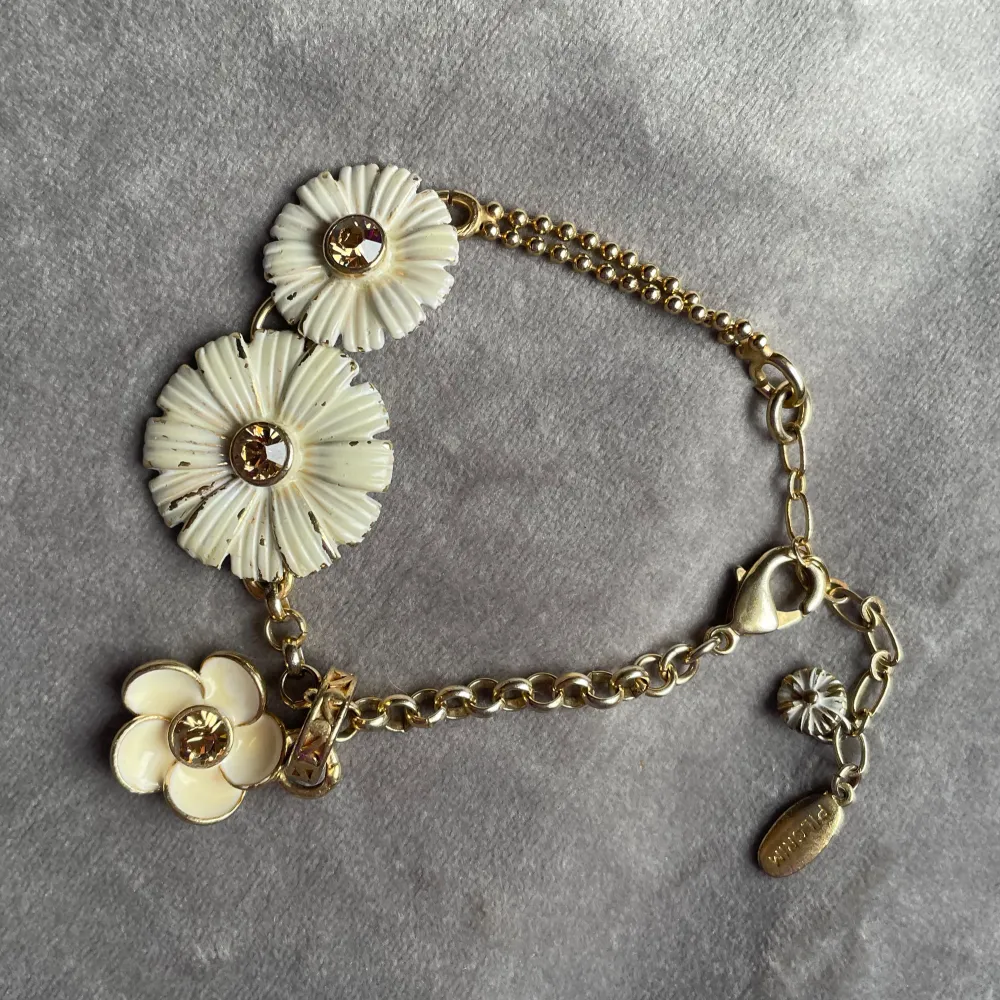 Säljer ett armband från Pilgrim med stora vita blommor och guldfärgade detaljer. Armbandet har en kedja i guldton och fina blomdetaljer med glittrande stenar i mitten. Perfekt accessoar för att lyfta din outfit!. Asusteet.