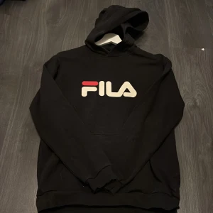 Svart hoodie från FILA - Säljer en svart hoodie från FILA med stor logga framtill i vitt och rött. Tröjan har huva och en stor magficka. Tröjan är välanvänd men ingenting som alls syns, skulle säga att storleken är xs/s