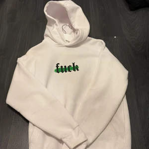 Vit hoodie från FSBN med tryck - Vit hoodie från FSBN i relaxed fit med svart och grönt tryck på bröstet. Stor luva och en stor ficka på magen. Använd en halv kväll samt den är lite större än en xs