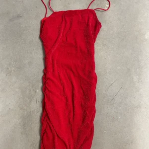 Röd glittrig långklänning med smala axelband & delvis öppen rygg - Säljer en röd långklänning med smala axelband och glittrigt tyg. Klänningen har en åtsittande passform och rynkade detaljer längs sidorna. Perfekt för festliga tillfällen när du vill sticka ut.