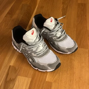 ASICS GEL grå och vita sneakers - Snygga ASICS GEL sneakers i vitt och grått med röda detaljer. Ovandel i mesh och mocka för en sportig vibe, med klassisk snörning och bekväm, stötdämpande sula. Perfekt skick, endast använda 1 gång. PRIS KAN DISKUTERAS - OBS: Box finns ej