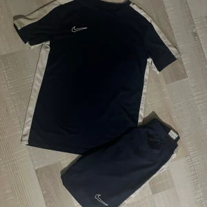Nike blå Dri-Fit tränings set  - Snygga marinblå träningsshorts från Nike i Dri-Fit material, perfekt för sport och aktivitet. Shortsen har elastisk midja och en vit Nike-logga framtill. Materialet är lätt och andas, vilket gör dem grymma för fotboll eller gym. Passar dig som gillar sportig stil. Man får med båda i priset! Ej hugget i sten