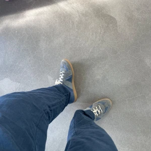 Blå och grå sneakers från Maison Margiela - Säljer ett par klassiska sneakers från Maison Margiela i blått och grått med vita snören och gummisula. Skorna har en mix av mocka och skinn, rund tå och platt sula. Perfekta för dig som gillar stilrena och tidlösa sneakers.Färgen pewter, dem enda äkta på marknaden. Har kvitto. Öppen till byten, men måste då gynna mig. Detta är en Intressekoll, kommer inte ge bort dem för låg pris