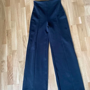 Svarta vida byxor från Nelly - Snygga svarta byxor från Nelly i storlek XS. De är högmidjade med vida ben och har en stilren look med pressveck framtill. Fint skick! Passar en både xs/s då dom är stretchiga