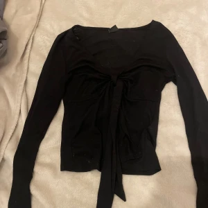 Svart croppad knytblus Gina Tricot XS - Svart långärmad croppad blus från Gina Tricot i storlek XS. Toppen har v-ringning och snygg knytning framtill som ger en trendig look. Perfekt att styla med jeans eller kjol för en cool outfit.