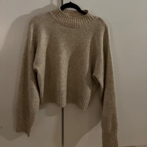 Beige stickad tröja  - Mysig beige stickad tröja från Monki i storlek XS. Tröjan har en hög ribbad krage och ribbade muddar vid ärmslut och nederkant. 