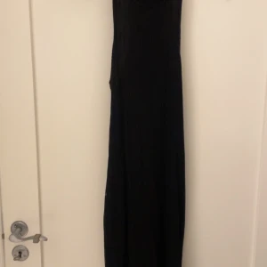 Svart ribbad långklänning BikBok XS - Svart långklänning från BikBok i storlek XS. Klänningen är ribbad och ärmlös med en tight passform och slits i sidan. Perfekt för dig som gillar en stilren och enkel look. Materialet är stretchigt och lätt, vilket gör den bekväm att bära.