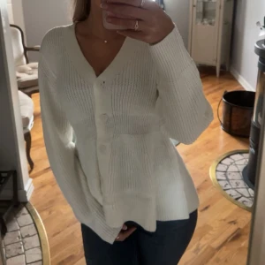 Vit stickad kofta med v-ringning - Superfin vit stickad kofta med v-ringning och stora knappar framtill. Modellen har långa ärmar och en lite lösare passform som ger en chill och snygg look. Perfekt att slänga på sig över ett linne eller t-shirt.