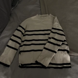 Randig beige stickad tröja Vero Moda - Snygg beige/vit stickad tröja från Vero Moda med svarta ränder. Tröjan har långärmade ribbade muddar och rund hals. Slit nere på tröjan💗ord pris: 450kr