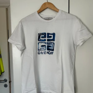 Vit Givenchy t-shirt med blått tryck - Snygg vit t-shirt från Givenchy med ett unikt blått grafiskt tryck och logga på bröstet. Klassisk rund hals och korta ärmar. Tillverkad i mjuk bomull som känns skön mot huden. Perfekt för dig som gillar stilrena designer med en twist.