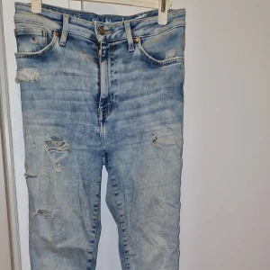 Ljusblå slitna jeans i storlek S/M - Säljer ett par ljusblå jeans med slitna detaljer och hål på benen. Jeansen har klassisk femficksmodell, knapp och dragkedja i gylfen samt bälteshällor. Perfekt för dig som gillar en avslappnad och trendig look. Storleken är S ,men det kan passa XS och M också 