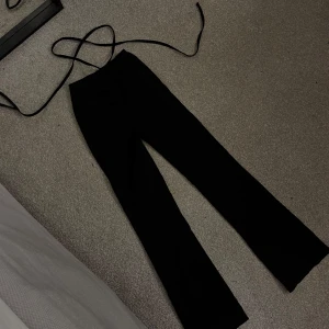 Svarta byxor med snörning i midjan - Snygga svarta byxor med långa ben och trendig snörning i midjan. Byxorna har en rak passform och är perfekta för dig som gillar en stilren look. Materialet känns mjukt och följsamt, vilket gör dem bekväma att bära hela dagen.