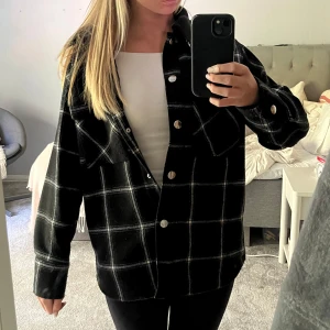 Svart rutig jacka från Monki - Säljer en svart och vit rutig höst jacka från Monki i storlek XXS. Jackan har klassisk krage, stora bröstfickor och silverfärgade knappar framtill. Perfekt att slänga över en hoodie eller t-shirt för en chill look.
