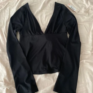 Svart långärmad topp från Nelly - Helt oanvänd, med prislapp kvar!!!         Svart långärmad topp från Nelly med djup v-ringning och snygg knytning i ryggen. 