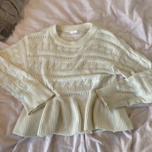 Vit stickad volangtröja Gina Tricot - Supersöt vit stickad tröja från Gina Tricot med volang nertill och snyggt hålmönster. Tröjan har rund halsringning, långa ärmar och ribbade muddar. Perfekt för dig som gillar en feminin och trendig look.