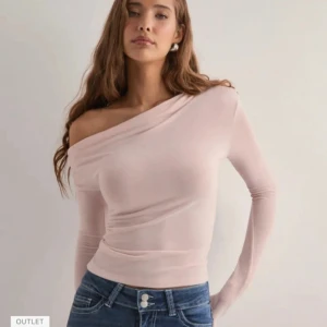 Ljusrosa offshoulder topp - Säljer en ljusrosa, tight offshoulder topp med lång ärm. Toppen har en snygg asymmetrisk skärning över axlarna och är figurnära med stretchigt material. Perfekt att styla med jeans eller kjol för en trendig look. Använd en gång inga defekter alls