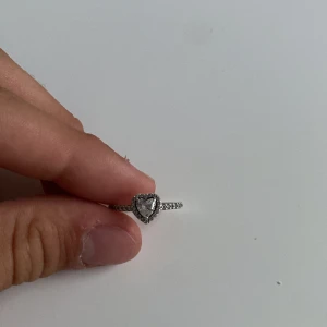 Pandora silverring med hjärta - Supersöt silverring från Pandora med ett glittrigt hjärta i mitten och små stenar längs hela ringen. Perfekt för dig som gillar romantiska detaljer och vill ha något som verkligen syns. Ringen är i äkta silver (S925) och har storlek 54.