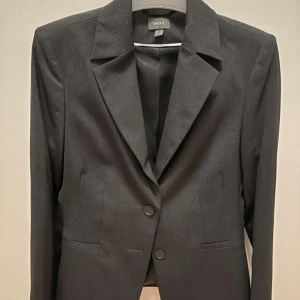 Mörkgrå kavaj från Mexx - Klassisk mörkgrå kavaj från Mexx. Kavajen har två knappar framtill, smala slag och två fickor. Snygg och stilren passform som funkar till många looks. Perfekt för dig som gillar en clean och tidlös stil