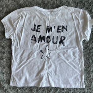 Vit t-shirt med tryck från Gina Tricot - Vit t-shirt från Gina Tricot med svart texttryck 'JE M'EN AMOUR' i storlek 158/164. Inte använd många gånger och i fint skick!🤍