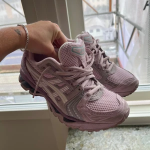 ASICS rosa sneakers med mesh och snörning - Säljer ett par snygga ASICS sneakers i ljusrosa med vita och grå detaljer. Skorna har mesh- och syntetpaneler, robust sula och klassisk snörning. Perfekta för dig som gillar sportig stil och vill ha bekväma skor med cool design. Något små i storleken