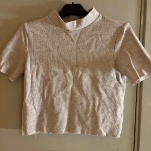Beige ribbad polotopp från Zara - Säljer en beige ribbad polotopp från Zara. Toppen har korta ärmar, hög krage. Perfekt att styla med jeans eller kjol för en clean look.