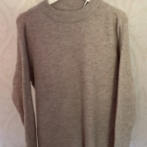 Beige ribbstickad tröja från ONLY - Supermjuk och ribbstickad beige tröja från ONLY. Klassisk rund halsringning och långa ärmar, perfekt för lager på lager. Enkel och stilren design som funkar till allt. Materialet känns riktigt cozy och passar dig som gillar en clean look.