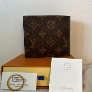 Brun luviton plånbok - Snygg plånbok från Luviton i klassiskt monogrammönster. Brun med ljusare luviton och blommor, tillverkad i skinn. Flera kortfack och fönster för ID. Kommer med originalask och certifikat.