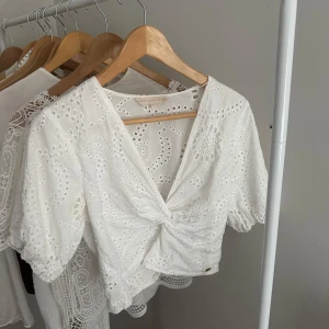 Vit broderad blus Pernilla Wahlgren - Superfin vit blus från Pernilla Wahlgren med broderade detaljer och knyt framtill. Blusen har v-ringning, korta puffärmar och är croppad. Perfekt för en fräsch och somrig look!