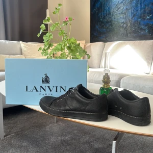 Lanvin skor - Stilrena svarta sneakers från Lanvin Paris i exklusivt skinn. Klassisk låg modell med rund tå, svarta snören och diskret branding på sulan. Skorna har en platt sula och levereras med originalbox och dustbags. Perfekta för dig som gillar minimalistisk och lyxig stil. Priset är ablout inte hugget i sten. 