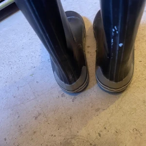 Mörkblåa gummistövlar med blå sula - Svarta höga gummistövlar med blå insida och blå mönstrad sula. Stövlarna har rund tå och vit rand längs sulan för en sportig look. Perfekta för regniga dagar och festivaler.