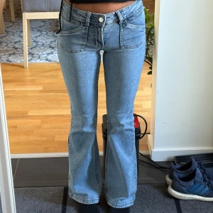 Bootcut jeans i ljusblå denim - Säljer ett par snygga bootcut jeans i ljusblå denim med klassiska fickor och dekorativa sömmar på bakfickorna. Jeansen har låg midja och är tillverkade i bomull med en skön passform. Perfekta för dig som gillar retrovibbar och vill ha ett par jeans med lite utsvängda ben. Storlek 32 men passar mig som bär 34💕