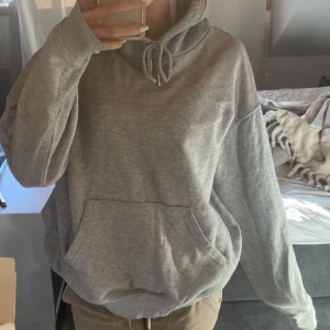 Grå hoodie med huva och ficka - Säljer en enkel grå hoodie från H&M i storlek M. Tröjan har en stor känguruficka framtill, snörning vid huvan och långa ärmar. Materialet är mjuk bomull och polyester, perfekt för chill dagar. Passformen är loose och färgen är ljusgrå. helt ny 