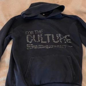 Mörkblå hoodie från Real Artistic People - Säljer en mörkblå hoodie i storlek S från Real Artistic People. Framsidan har texten 'FOR THE CULTURE' i silvriga nitar och en cool definition under. På ärmen finns ett broderat vitt grafiskt mönster och baktill står 'REAL ARTISTIC PEOPLE' broderat. Hoodien har huva och magficka. ⚠️den är fejk⚠️ Några diamanter som lossnat annars fint skick🩷