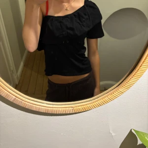Svart oneshoulder topp med volang - Säljer en svart oneshoulder topp med volangdetalj längs halsringningen. Toppen är croppad och har en ärm, är hemmasydd. Passar mig som har storlek xs/s🩷