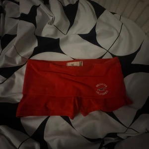 Röda Hollister shorts med logga - Snygga röda shorts från Hollister med vit logga på sidan. Modellen är lågmidjad och tight, perfekta för träning eller chill. Mjukt bomullsmaterial som sitter skönt och följer kroppen. Kort passform som visar benen och ger en sportig vibe.