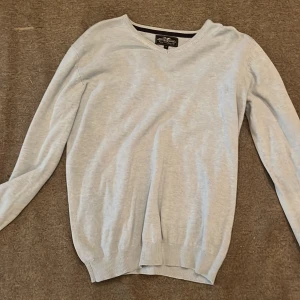 Ljusgrå v-ringad tröja Hampton Republic - Säljer en stilren ljusgrå v-ringad tröja från Hampton Republic. Tröjan har lång ärm, ribbade muddar och är i ett mjukt material som passar perfekt till lager-på-lager. Enkel och clean design som funkar till många outfits.