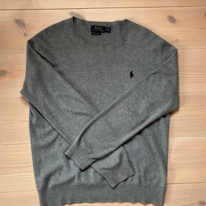 Grå bomullströja från Polo Ralph Lauren - Snygg grå tröja från Polo Ralph Lauren i mjuk pima bomull. Klassisk rund halsringning och diskret broderad logga på bröstet. Perfekt basic med lång ärm och ribbade muddar för en clean och stilren look. Priset kan diskuteras vid snabb affär