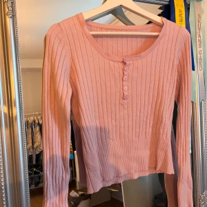 Rosa ribbad långärmad tröja - Säljer en söt ljusrosa ribbad tröja med lång ärm och rund halsringning. Tröjan har knappar framtill och är figurnära med stretchigt material. Perfekt för lager-på-lager och passar till både jeans och kjol. Den är väldigt stretchig, skulle säga att den passarungefär alla storlekar!💕😸