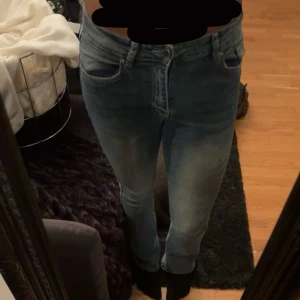 Blå jeans med strassdetaljer bak - Säljer ett par ljusblå jeans med snygg tvätt och raka ben. Byxorna har lite hög midja och bakfickor med strass och broderade detaljer som ger extra edge. Klassisk femficksmodell i stretchig denim som sitter riktigt bra.