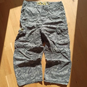 Dickies camouflage cargopants  - Säljer ett par grå camouflage cargoshorts från Dickies med flera stora fickor på sidorna och bak. Klassisk Dickies-logga och coolt gult tryck på insidan av linningen. Perfekta för dig som gillar streetwear och praktiska detaljer. Äkta. Mer information, bilder och prisdiskutering i dm. True skate jeans. 