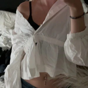 Vit blus från Weekday - Säljer en vit omlottblus från Weekday i storlek S. Blusen har v-ringning, långa puffiga ärmar med resår vid handlederna och resår i midjan. Tillverkad i tunn bomull, perfekt för en trendig och luftig look. Passformen är loose och modellen är croppad. Den går även att knäppa igen fram till 🤍