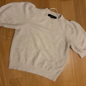 Beige stickad tröja Vero Moda XS - Superfin beige stickad tröja från Vero Moda i storlek XS. Tröjan har puffiga korta ärmar och ribbade muddar vid hals, ärmslut och nederkant. Perfekt för dig som gillar en söt och trendig look med lite volym på axlarna.