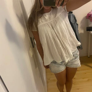 Vit blus med broderad överdel - Söt vit blus med korta ärmar och broderad överdel. Blusen har en luftig och flowy passform med fina spetsdetaljer vid ärmslut och halsringning. Perfekt för en fräsch och somrig look.