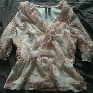 Prickig omlottblus med volanger - Säljer en söt och luftig omlottblus från H&M med volangdetaljer och v-ringning. Blusen är vit med prickigt mönster i rosa, rött och gult, har trekvartsärm och är gjord i ett tunt, transparent material som känns riktigt somrigt.