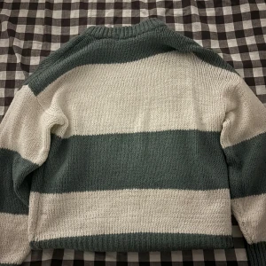 Randig stickad tröja i grönt och vitt - Säljer en mysig stickad tröja med breda ränder i mörkgrönt och vitt. Tröjan har långärmade och en klassisk rund halsringning. Perfekt för dig som gillar chill och enkel stil med lite retrovibe.