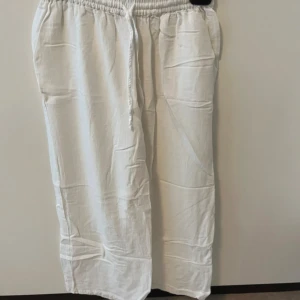 Vita linnebyxor från Nelly med snörning - Säljer ett par fräscha vita linnebyxor från Nelly i storlek 32. Byxorna har elastisk midja med snörning och raka, loose ben. Perfekta för chill dagar och sommarhäng. Materialet är linne som ger en skön och luftig känsla. (Gammal bild på sista bilden) 