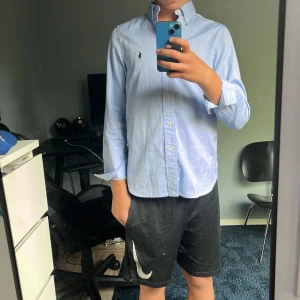  Ralph Lauren skjorta  - Snygg ljusblå skjorta från Ralph Lauren i slim fit-modell. Klassisk button-down krage, broderad logga på bröstet. Den är använd ca 10 gånger köpt förra året. Jag är 167 och den sitter lite tajt och är kort i armarna 